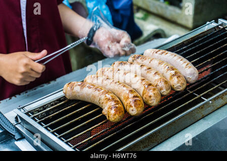 Saucisses fraîches et des hot-dogs sur le gril en plein air sur un barbecue à gaz. Banque D'Images