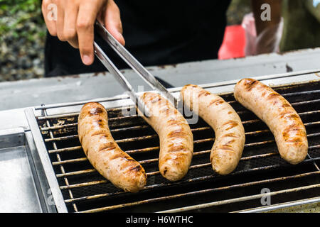 Saucisses fraîches et des hot-dogs sur le gril en plein air sur un barbecue à gaz. Banque D'Images