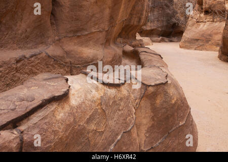 Vue sur le canal d'eau de coupe de roche utilisé pour apporter l'eau du printemps à Wadi Musa par le passage étroit de Siq dans l'entrée de roche rouge aux ruines de Petra l'ancienne capitale du Royaume nabatéen dans le désert sud-ouest de Jordanie Banque D'Images