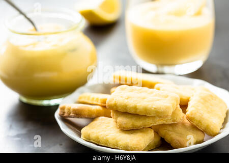 Des biscuits sur une soucoupe blanc et le lait caillé de citron dans un bocal en verre Banque D'Images