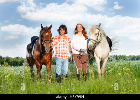 Jeune couple aimant la marche avec les chevaux dans un champ Banque D'Images