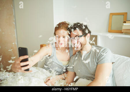 Couple couvert de plumes pillow fight en tenant au lit selfies smartphone Banque D'Images