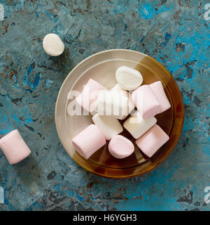 Guimauves blanches et roses dans un bol en céramique bleu sur fond de béton. Vue d'en haut. Banque D'Images