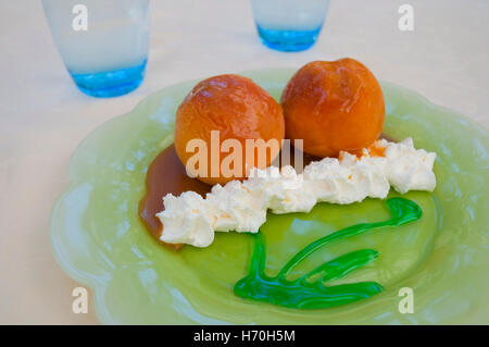 Dessert : deux pêches au four avec de la crème chantilly, sauce caramel et menthe poivrée. Banque D'Images