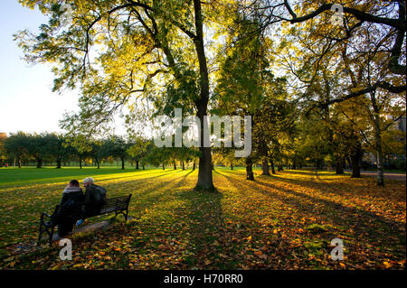 Les visiteurs sur un banc de parc dans les prés, Édimbourg, Écosse que la faible lumière du soleil l'automne projettent de grandes ombres à travers les arbres. Banque D'Images