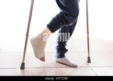 Jeune homme avec une cheville cassée et un blanc moulé sur sa jambe, marcher avec des béquilles (isolé sur blanc) Banque D'Images