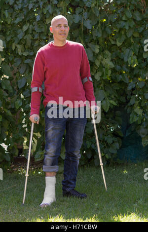 Jeune homme avec une cheville cassée et un plâtre en fibre de verre blanc et sur sa jambe, obtenir un peu d'air frais dans le jardin pendant que wal Banque D'Images