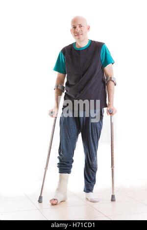 Jeune homme avec une cheville cassée et une fibre de verre et en plâtre à la jambe, appuyé sur ses béquilles (isolé sur blanc, plein d'adm. Banque D'Images