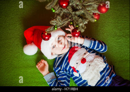 Heureux petit garçon est située près de sapin. Les jours fériés. dans un T-shirt à rayures avec le Père Noël Banque D'Images