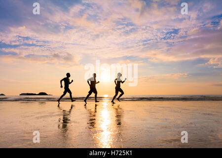 Groupe de trois coureurs s'exécutant sur une plage en été au coucher du soleil - Notion sur les saines habitudes de vie sportive et communautaire Banque D'Images