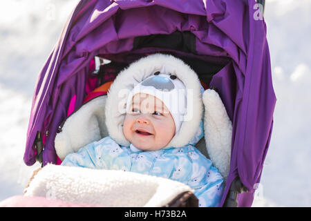 Funny laughing baby sitting dans une poussette sur c vieux jour d'hiver Banque D'Images