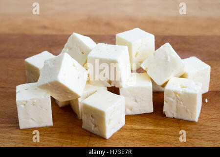 Cubes carrés de fromage féta isolé sur bois board avec couteau. Banque D'Images