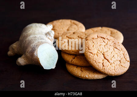 La racine de gingembre frais, à côté d'une pile de biscuits au gingembre isolé sur bois foncé. Banque D'Images