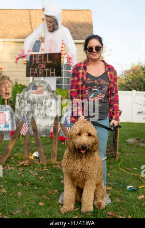 Bellmore, New York, USA. 2e Nov, 2016. Corinne, de Wantagh, et son Jax Goldendoodle sont debout dans la cour avant de Fuscaldo Eileen avec un cimetière avec un grand affichage, Hillary Clinton Ghost avec ''l'enfer sur terre''), ainsi que des pierres tombales avec des photos d'Américains tués à Benghazi. Credit : Ann Parry/ZUMA/Alamy Fil Live News Banque D'Images