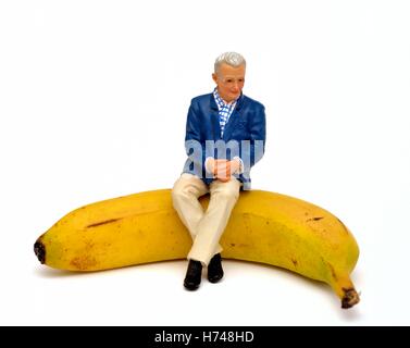 Une figurine homme retraité assis sur une banane. Banque D'Images