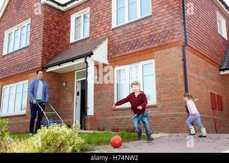 Les enfants jouent dans le jardin comme père tond pelouse à l'extérieur chambre Banque D'Images