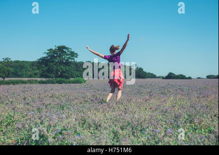 Une jeune femme saute autour dans un champ de fleurs violettes sur une journée ensoleillée Banque D'Images