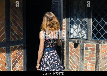 Une jeune femme portant une robe est l'ouverture d'une porte et entre dans une vieille ferme rustique à l'été Banque D'Images