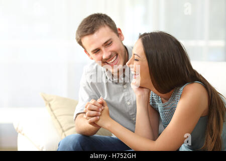 Couple heureux ou mariage à l'autre rire et tenir la main assis sur un canapé à la maison Banque D'Images