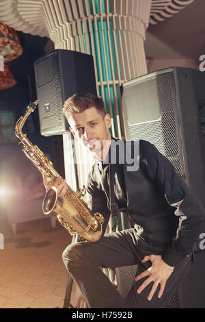 Jeune homme assis et holding saxophone Banque D'Images