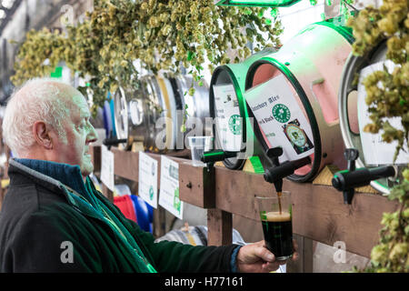 L'Angleterre, Tunbridge Wells. La bière et l'ale CAMRA festival. Couple et verser une pinte de bière à partir de la bière le baril, tonneau, parmi beaucoup d'autres barils. Banque D'Images