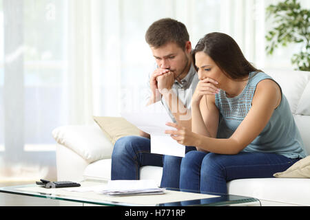 Young couple lire un avis important dans une lettre assis sur un canapé dans la salle de séjour à la maison Banque D'Images