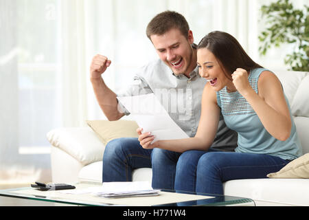 Couple excité la lecture d'une lettre, assis sur un canapé dans la salle de séjour à la maison Banque D'Images