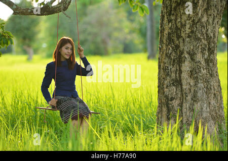 Femme assise sur une balançoire dans un champ, Thaïlande Banque D'Images