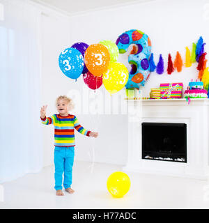 La célébration de l'enfant troisième anniversaire. Petit garçon présente l'ouverture et la tenue des ballons dans la salle décorée. D'anniversaire pour les enfants. Banque D'Images