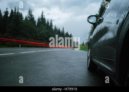 Des sentiers et des feux de véhicule automobile sur la route humide. Temps de pluie. Selective focus, une longue exposition de droit. Banque D'Images