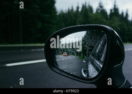 Gouttes de pluie sur le côté de la voiture et le rétroviseur extérieur de voiture la réflexion. La route et l'arrière-plan sur la forêt Banque D'Images