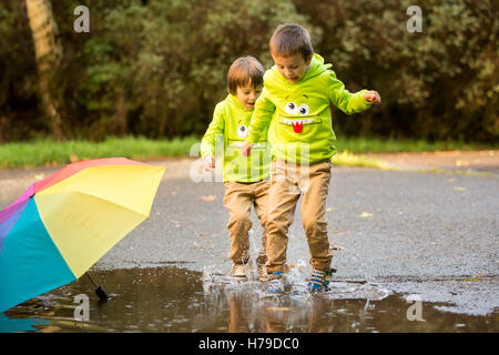 Deux adorables petits garçons avec parapluie dans un parc un jour de pluie, jouant et sautant, sourire, parler ensemble, autumntime Banque D'Images