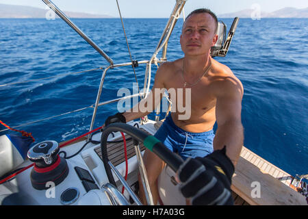 Jeune homme skipper steers voile yacht à voile sur l'océan. Banque D'Images