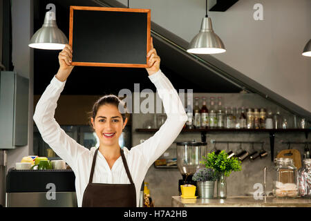 Belle Caucasian woman holding tablier barista dans tableau noir vide à l'intérieur inscription coffee shop - prêt à insérer du texte Banque D'Images