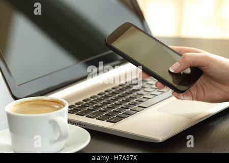 Close up of a lady part des messages sur un téléphone intelligent avec un ordinateur portable dans l'arrière-plan dans un bureau à domicile ou office interior Banque D'Images