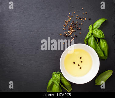 Dans un bol d'huile d'olive, basilic frais, poivre noir et coriandre sur une ardoise noire avec une copie de l'espace, vue d'en haut Banque D'Images