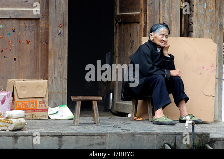 Une vieille femme Dong assis devant sa maison en bois dans village Zhaoxing, dans la province de Guizhou, Chine Banque D'Images