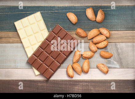 Gros plan d'une bande d'amandes brutes dans leurs coquilles et les bars de lait et chocolat blanc sur fond de bois Banque D'Images