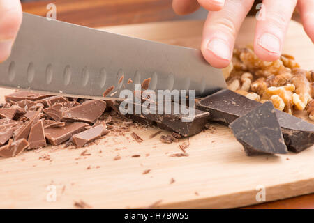 Hacher au couteau Chef chocolat sur une planche à découper. La préparation des desserts en cuisine avec la lumière et le chocolat noir. Banque D'Images