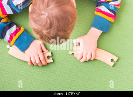 Enfant jouant avec des voies de chemin de fer en bois. L'assemblage de deux pièces. Concept de l'apprentissage de la petite enfance et la résolution de problèmes. Banque D'Images