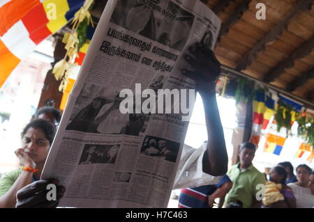 Un homme est en train de lire un journal, la queue pour de la nourriture gratuite dans un temple hindou à Kandy, Sri Lanka, le jour de la fête du Vesak. Banque D'Images