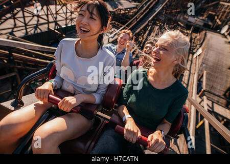 Shot of young people riding un roller coaster. Les jeunes femmes et les hommes s'amusant sur amusement park ride. Banque D'Images