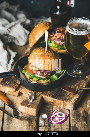 Des hamburgers avec bacon croustillant et légumes en petite casserole et verre de bière de blé rustique servant plus de conseil sur shabby Banque D'Images