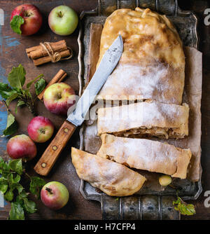 Tranches de strudel aux pommes fait maison servi avec des pommes fraîches avec des feuilles, des bâtons de cannelle et le sucre en poudre sur le plateau métallique vintage avec Banque D'Images