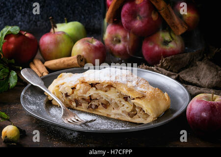 Tranches de strudel aux pommes fait maison servi avec des pommes fraîches dans un bocal en verre, des bâtons de cannelle et le sucre en poudre sur vintage plaque metal wit Banque D'Images