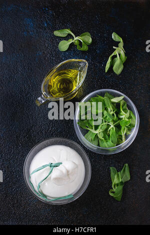 Ensemble de fromage italien lié à la saumure de burrata servis avec salade de maïs frais et d'huile d'olive en plus de coupes en verre textures sombres backgrou Banque D'Images