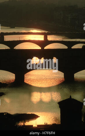 Ponts sur l'Arno illuminée par un coucher de soleil tout en Ponte Vecchio fait de l'ombre sur la rivière Banque D'Images