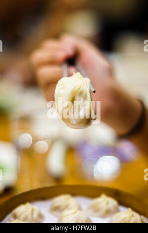 Dim sum chinois rempli de soupe dumpling xiao long bao tenu par une paire de baguettes. Focus sélectif. Banque D'Images