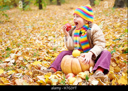 Petite fille en forêt d'automne, s'asseoir sur des feuilles jaunes, de manger et de citrouille apple Banque D'Images