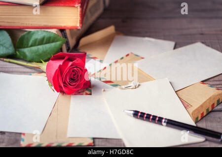 Enveloppes vintage, rose rouge et de feuilles de papier éparpillées sur la table en bois pour l'écriture des lettres. romantique Banque D'Images